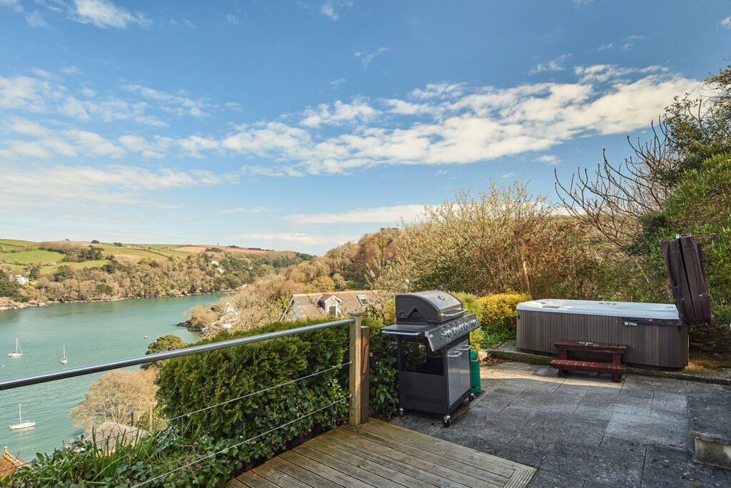 Outdoor patio with grill, hot tub, and view of a river and countryside on a sunny day.